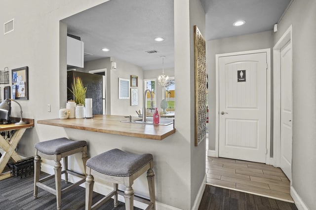 Open kitchen bar with two stools, sink, and a doorway to a restroom.