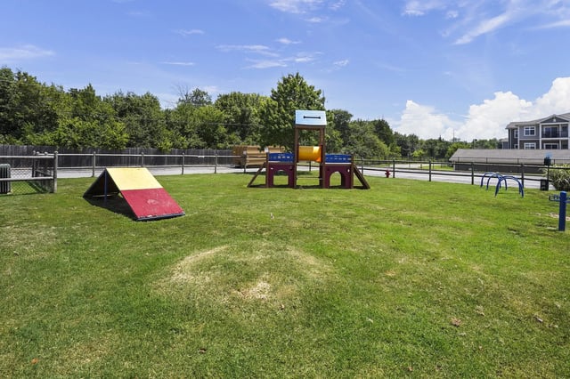 Playground on a grassy lawn with a colorful play structure inside a fenced area.