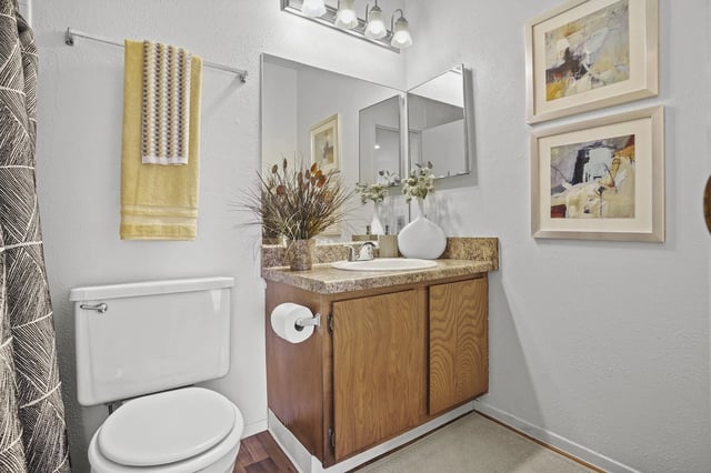 Apartment bathroom with toilet, wood vanity, marble countertop, and two framed mirrors.