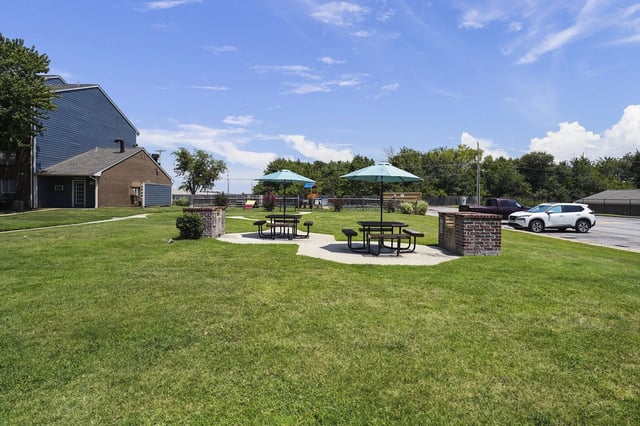 Outdoor community space with picnic tables, umbrellas, and a small playground in the background.