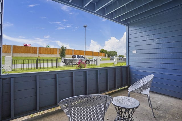 Blue exterior balcony with metal chairs and a round table overlooking a street.
