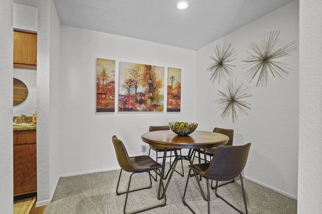 Small dining area with round wooden table and four brown chairs in an apartment unit.