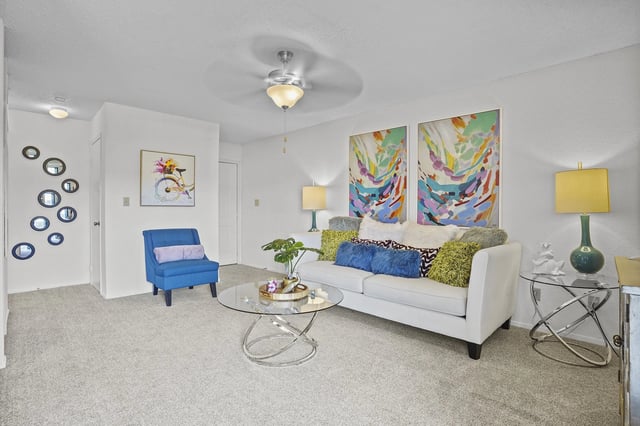 Living room with white sofa, blue accent chair, glass coffee table, and colorful abstract wall art.
