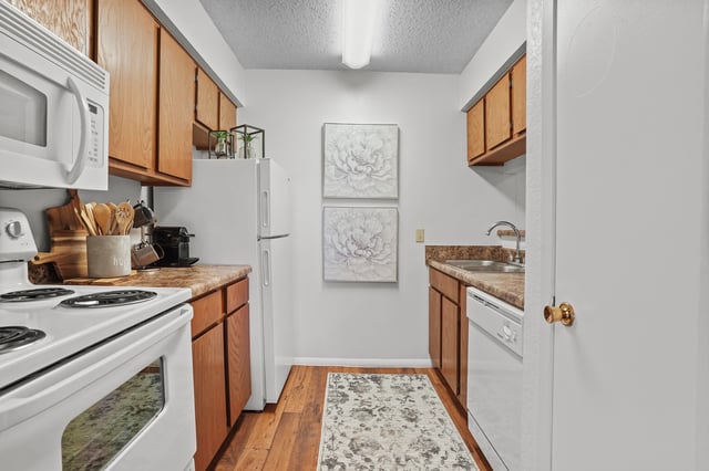Kitchen with wooden cabinets, white appliances, and floral wall art.