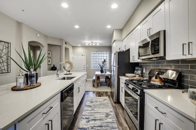 Modern kitchen with white countertops, cabinets, stainless steel appliances, and a dining area.