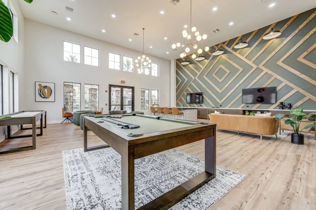 Spacious community lounge with a pool table, shuffleboard, bar seating, and lounge area.