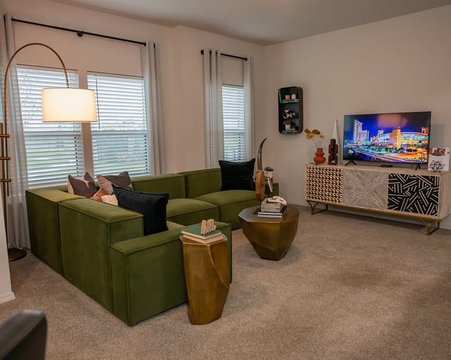 Modern living room with a large green sectional sofa, geometric coffee table, and a TV displaying a city skyline.