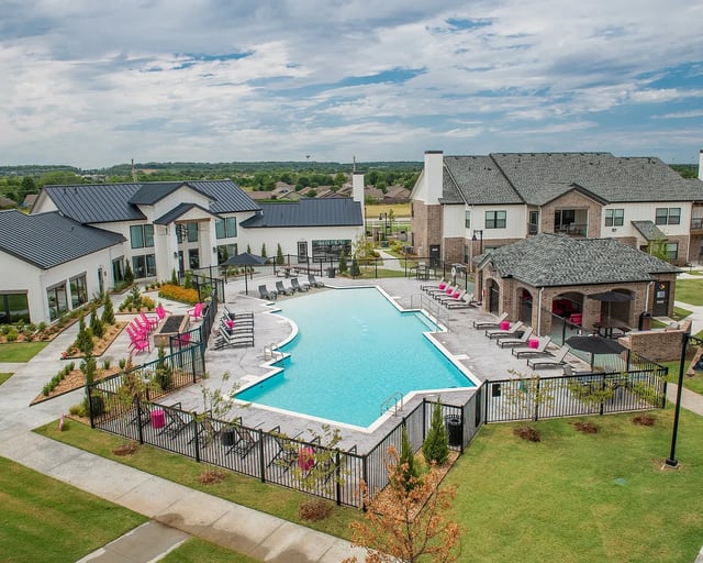 Aerial view of a resort-style apartment pool with lounge chairs and surrounding buildings.