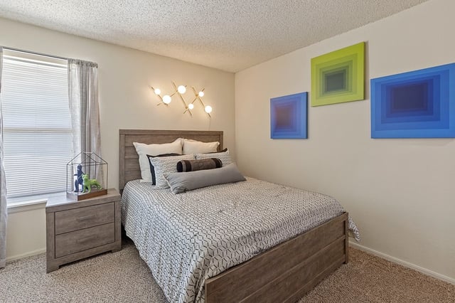 Modern bedroom with a gray wood bed frame, nightstand, blinds, and abstract square wall art.
