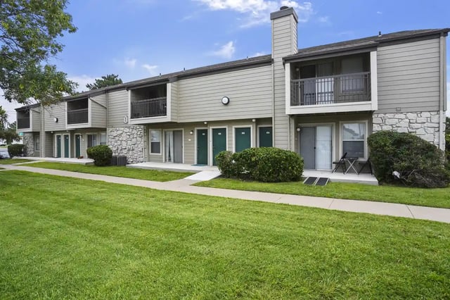 Exterior view of a two-story apartment building with balconies and a green lawn.