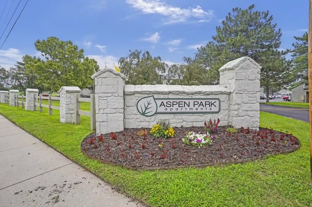 Stone entrance sign reading Aspen Park Apartments with landscaped flower bed.