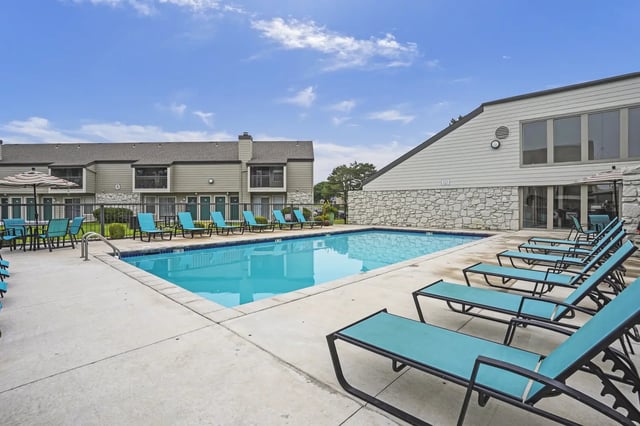 Outdoor pool with turquoise lounge chairs in an apartment community courtyard.