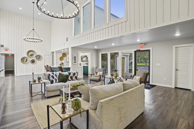 Bright, open resident lounge with white panel walls, circular chandeliers, and comfortable seating.