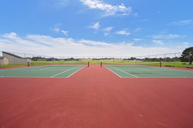 Tennis courts with red and green surfaces under a blue sky with clouds.