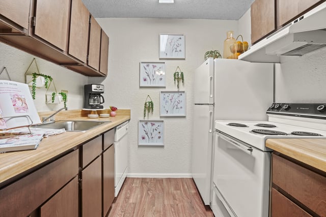 Kitchen with dark wood cabinets, white countertops, stainless steel sink, coffee maker, and white appliances.