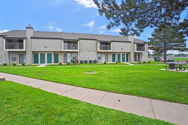 Exterior of apartment building with manicured lawn and picnic tables.