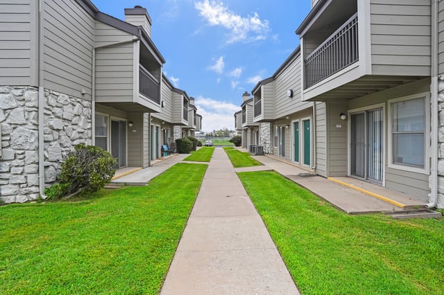 Exterior view of apartment buildings with a walkway and grass.