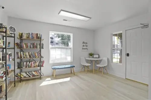 Community book exchange and lounge area with shelves of books, a small table with chairs, and a window.