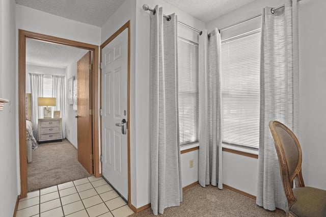 A room with a chair and a bed in the background.