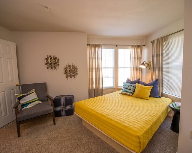 A bedroom with a yellow bed and a grey chair.