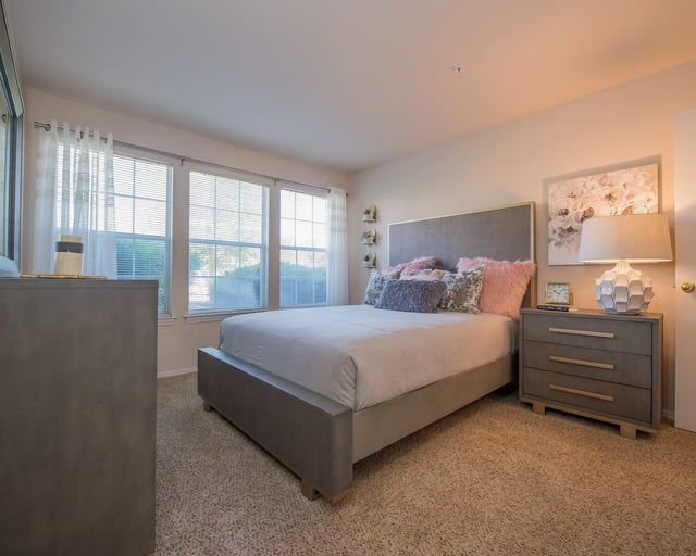 A bedroom with a large bed, a nightstand, and a window with curtains.