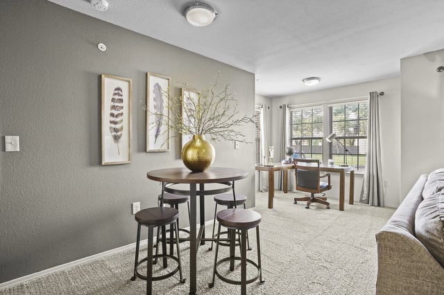 A round table with four stools and a vase of branches on it, with a desk and chair in the background.