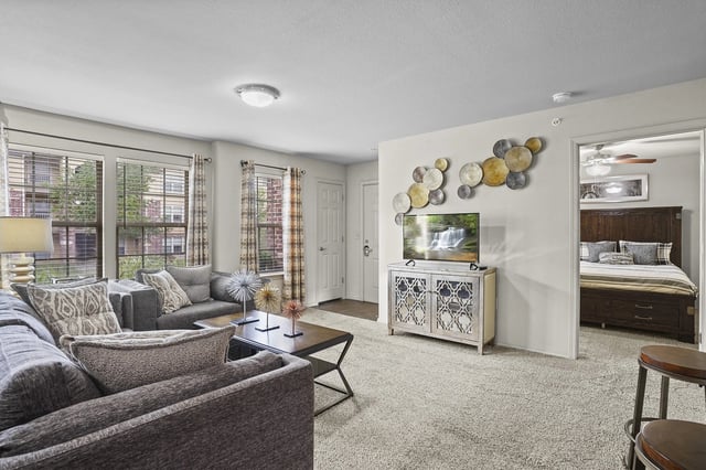 Living room with a sofa, coffee table, and TV, leading into a bedroom.