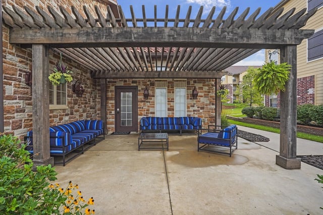 Outdoor patio with wooden pergola, comfortable seating, and stone accent walls.