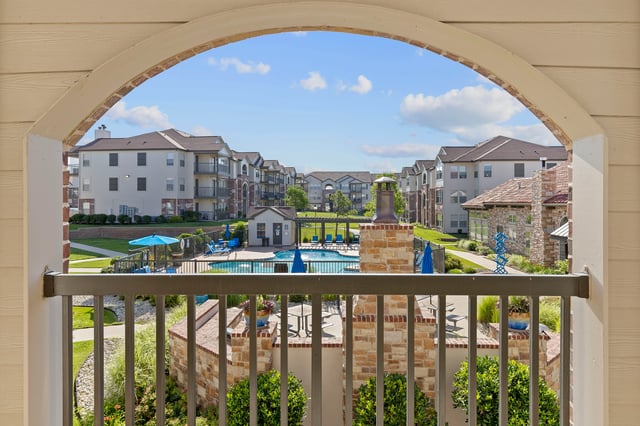 View of a resort-style swimming pool with lounge chairs and umbrellas, surrounded by apartment buildings.