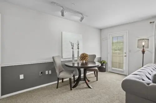 Dining area with a round table and two chairs, next to a living room couch and a door leading outside.