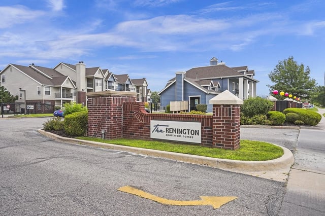 Brick entrance sign for The Remington apartment homes with blue buildings in the background.