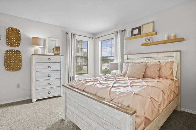 Bedroom with light wood bed frame, dresser, and two windows with curtains.