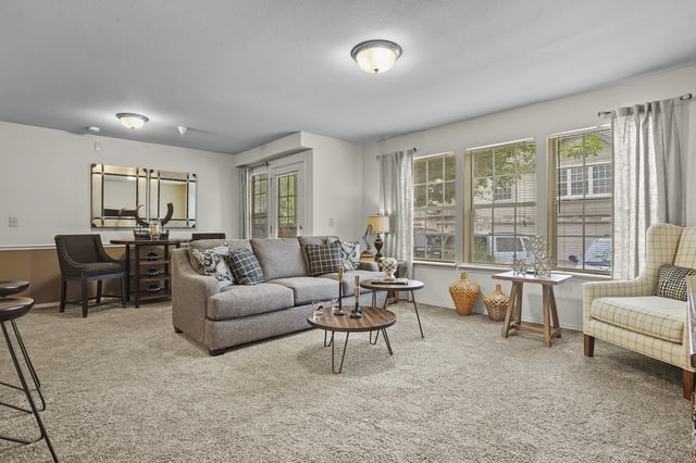A living room with a grey couch, a chair, a table, and a mirror.