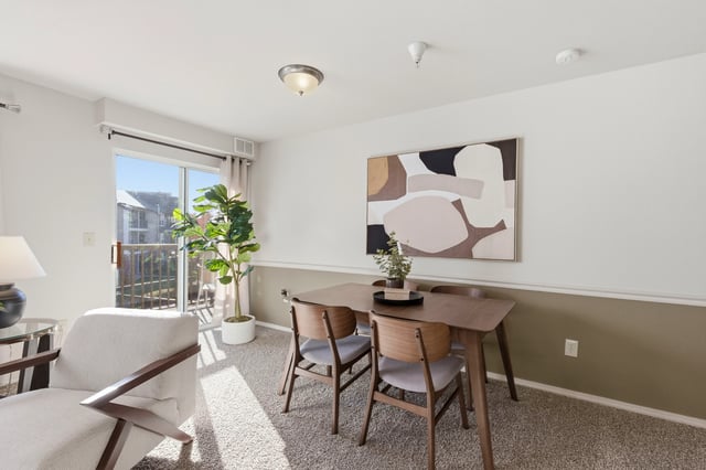 Dining area with table and chairs, next to a sliding glass door with a balcony view.