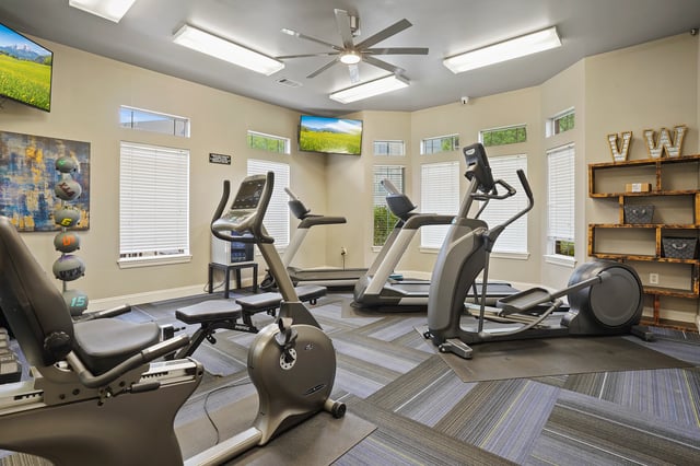 Gym with treadmills, stationary bikes, and elliptical machines, featuring TVs on the wall.