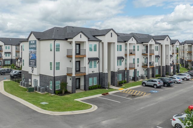 Exterior view of a modern apartment building with a 'Now Leasing' banner.