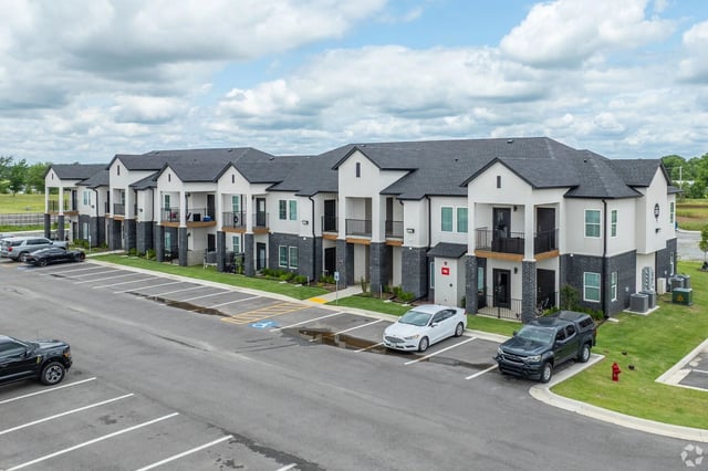 Exterior view of a modern apartment community with connected buildings, balconies, and a parking lot.