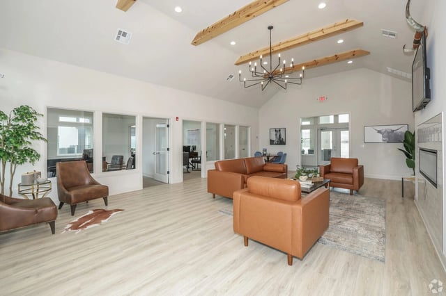 Bright resident lounge with tan leather seating, coffee table, plants, and exposed wooden ceiling beams.