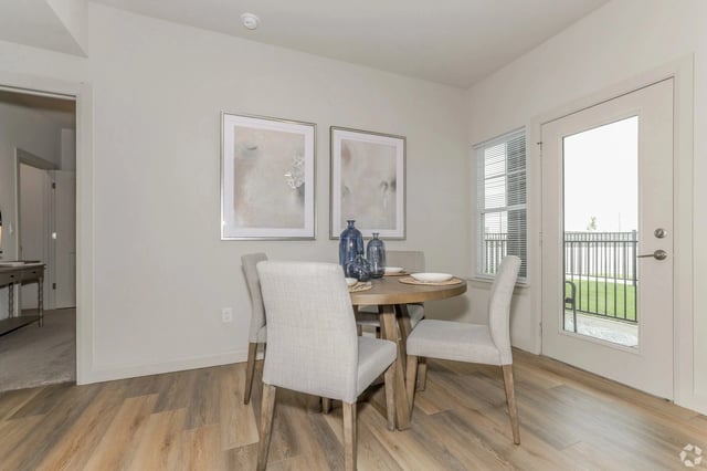 Dining area with a round wooden table and four beige upholstered chairs near a glass door to a balcony.