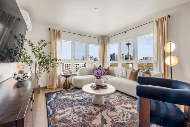Bright living room in a modern apartment with large windows and a curved white sofa.