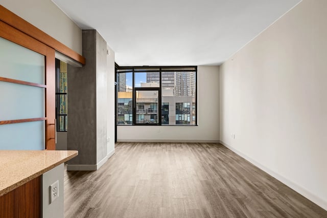 Interior view of an unfurnished apartment living space with large windows overlooking a city skyline.