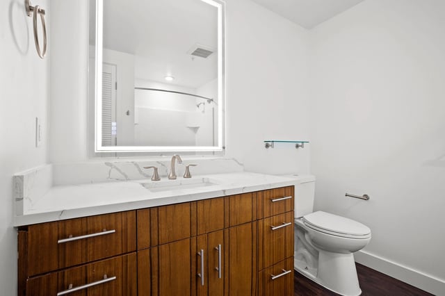 Bathroom with a wood vanity, marble countertop, LED mirror, and toilet.