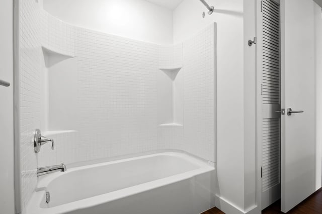 Modern bathroom with white tiled shower and tub combo, chrome fixtures, and a closed door.