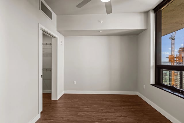 Empty bedroom with a closet and a large window overlooking a city construction site.