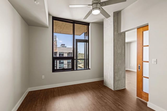 Empty bedroom with hardwood floors and a large window overlooking the city.
