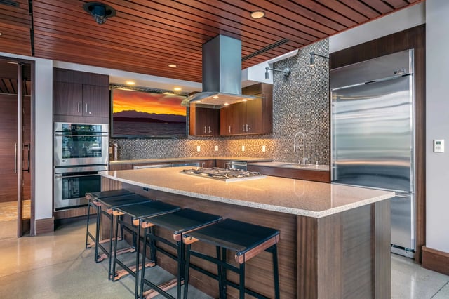 Modern kitchen with large island, stainless steel appliances, and a TV.