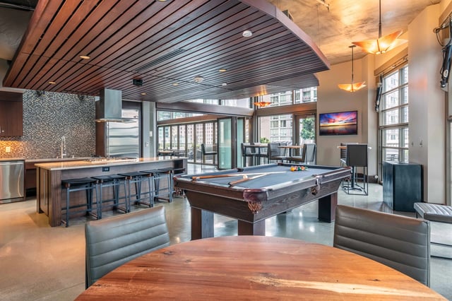 Pool table and kitchen island with bar stools in a modern apartment common area.