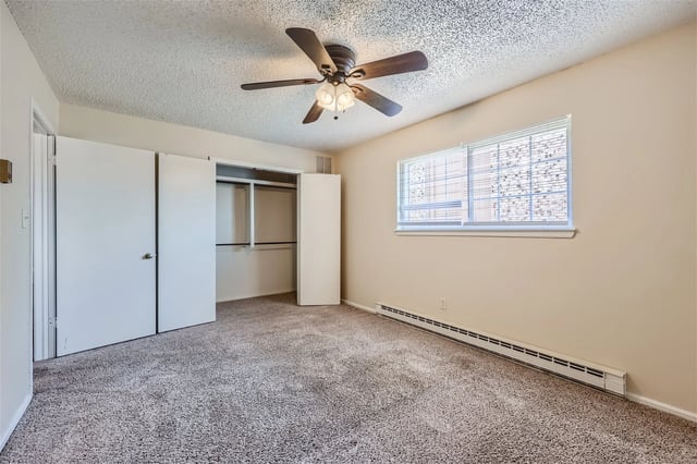 Bedroom with ceiling fan, beige walls, carpeted floor, and open closet.