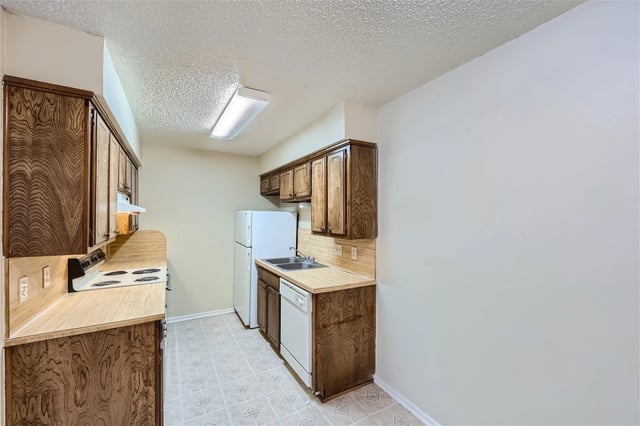 Galley-style kitchen in an apartment with wood cabinets, beige countertops, a sink, range, fridge, and dishwasher.