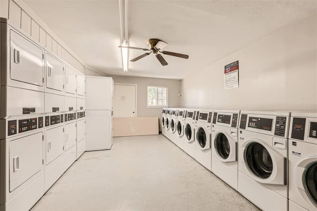 Public laundry room with stacked dryers on the left and front-loading washers along the right wall.